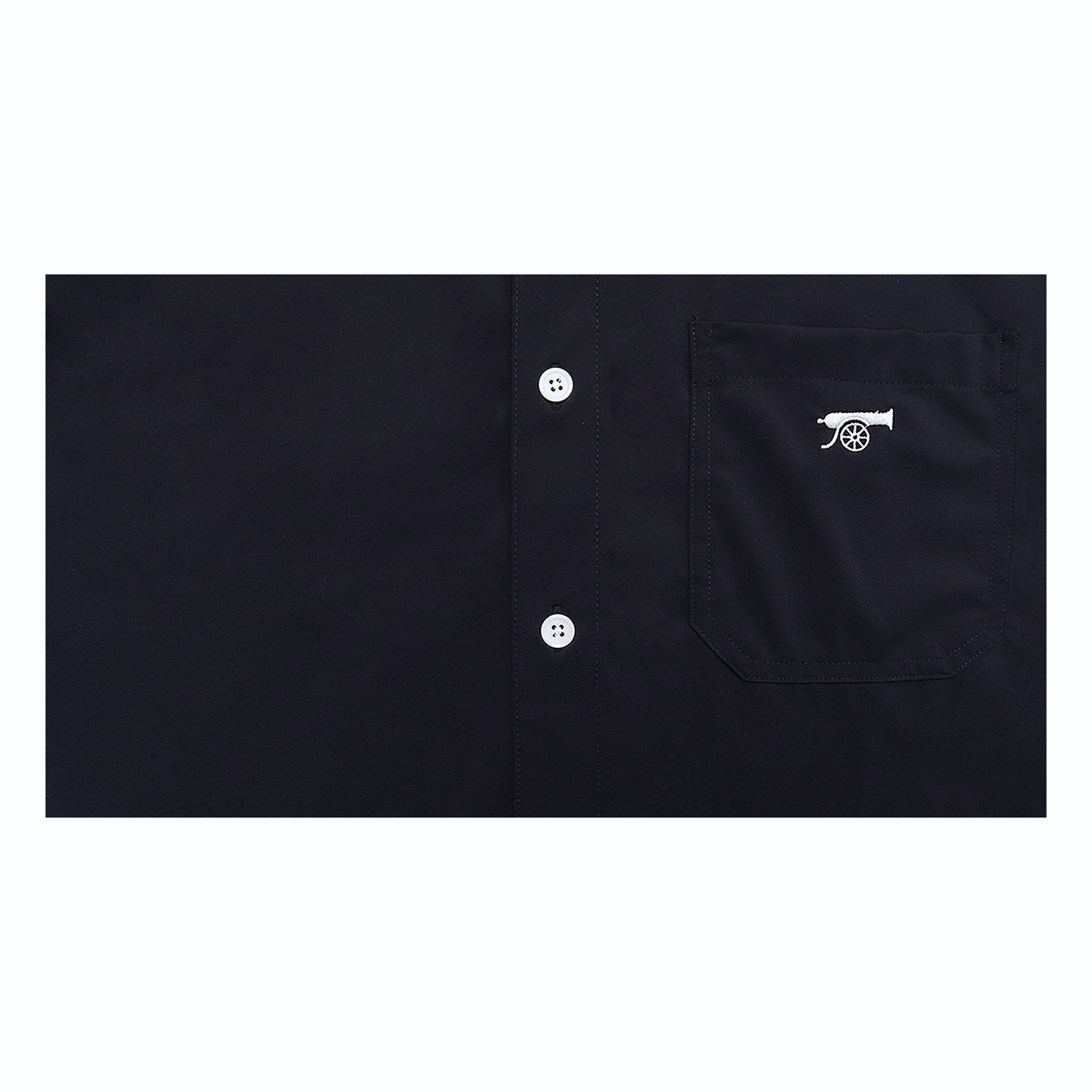 Close-up of a dark navy button-up shirt showing the front pocket with a small white embroidered cannon logo and white buttons.